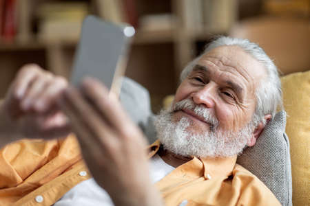 Relaxed elderly man using smartphone while resting at home