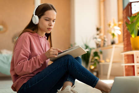 Smart focused schoolgirl with educational materials, books and laptop working on school project at homeの写真素材