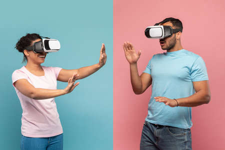 Young black spouses in VR headset touching air during virtual reality experience, blue and pink studio backgroundの写真素材