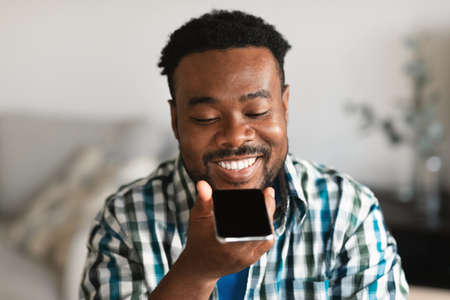 Cheerful African Man Using Voice Search On Smartphone At Homeの写真素材