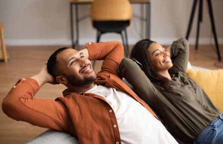 Relaxed Black Couple Sitting On Couch Relaxing Together At Homeの写真素材
