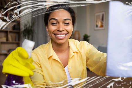 Black Woman Cleaning Window Glass With Rag And Detergent Indoor