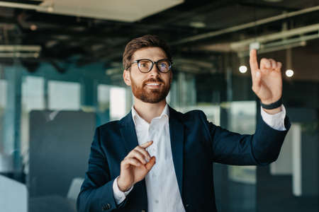 Successful entrepreneur in formalwear selecting something on virtual screen, standing in modern office interior, mockupの写真素材