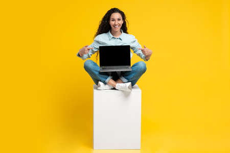 Happy Middle Eastern Lady Showing Laptop Screen On Yellow Backgroundの写真素材