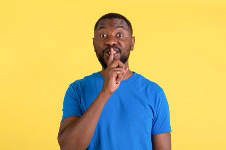 African American Man Gesturing Hush Sign Posing Over Yellow Backgroundの写真素材