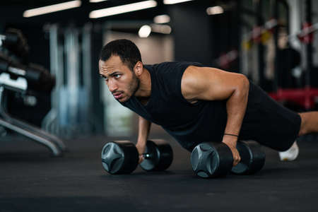 Muscular Man Making Dumbbell Push-Ups Exercise At Gym