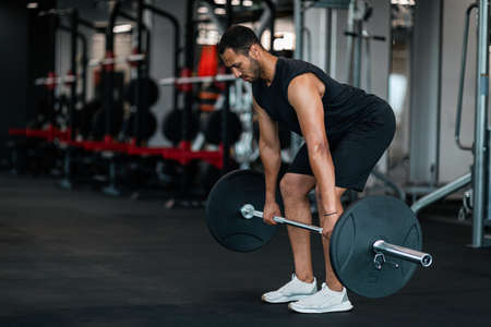Sporty Black Man Lifting Heavy Barbell While Training At Gymの写真素材