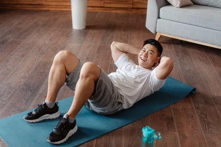 Full length of active middle aged man strengthening core muscles, doing abs exercises at home on...