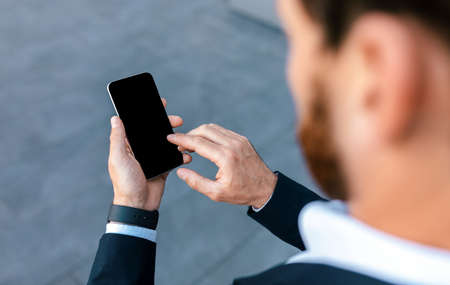 Confident millennial businessman with beard in suit chatting on phone with blank screen