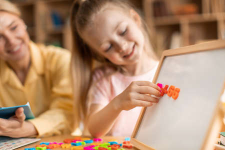 Happy cute girl learning alphabet, cheerful female child development specialist working with smiling...