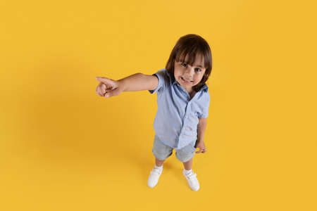 Top view portrait of cute little boy pointing aside at free space and smiling, yellow studio backgroundの写真素材