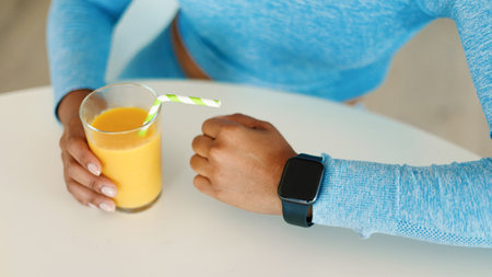 Healthy lifestyle concept. Unrecognizable sporty lady wearing smart watch and holding glass of fresh juiceの写真素材