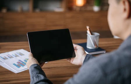 Adult japanese man have video call on tablet with blank screen at table in office interior, backの写真素材