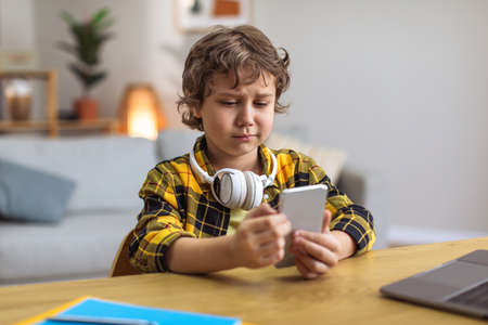 Little displeased boy looking sadly at smartphone, losing video game or reading unpleasant message,...