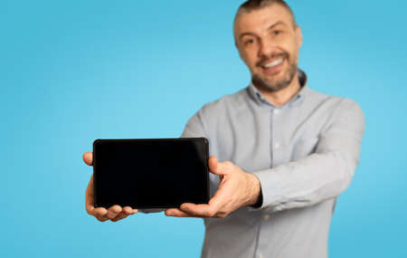 Cheerful Man Showing Mobile Phone With Blank Screen, Blue Backgroundの写真素材