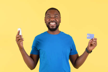 African Man Holding Cellphone And Credit Card Shopping, Yellow Background