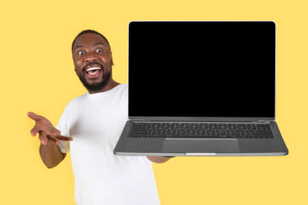 Excited African American Male Showing Laptop Computer Over Yellow Backgroundの写真素材