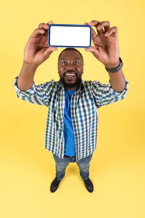 African American Male With Smartphone Showing Screen, Yellow Background, Vertical