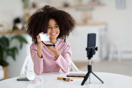 Black preteen girl doing makeup and recording vlog on phoneの写真素材