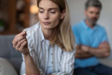 Unhappy sad adult caucasian wife holding ring and ignoring disappointed man in living room interior,...