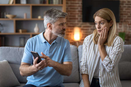 Unhappy adult caucasian man with beard shows phone to shocked lady, woman suffers from gadget...