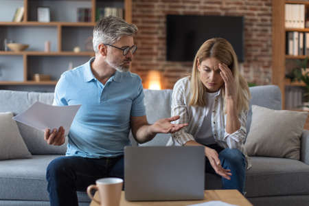 Unhappy sad senior caucasian man and woman work with documents and laptop, pay taxes and quarrel