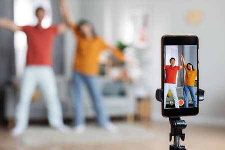 Funny asian husband and wife recording video, using smartphone