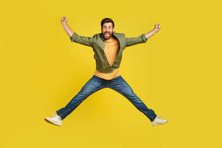 Expressing happiness. Full length studio shot of excited middle aged man jumping over yellow backgroundの写真素材
