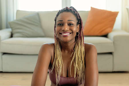 Portrait of happy african american woman in sports clothes taking break from home workout and...