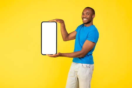 Black Man Holding Big Phone With Empty Screen, Yellow Backgroundの写真素材