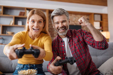 Glad excited adult caucasian female and male with joysticks play in online game in free time,...