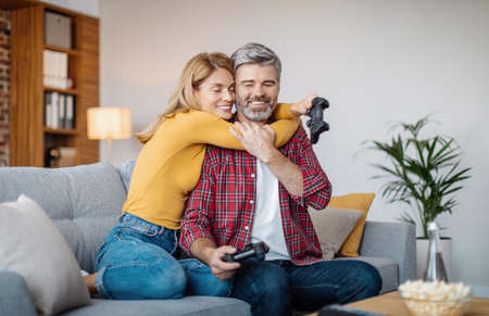 Smiling middle aged caucasian wife hugging husband with joystick, celebrating victory in online game