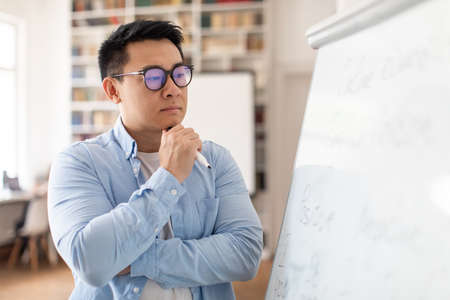 Thoughtful Asian Man Teacher Thinking Looking At Whiteboard In Classroomの写真素材