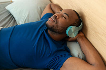 Black Guy Wearing Earphones Listening To Music Relaxing In Bedroomの写真素材