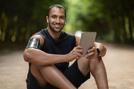 Positive black guy using digital pad while having workout outdoorsの写真素材