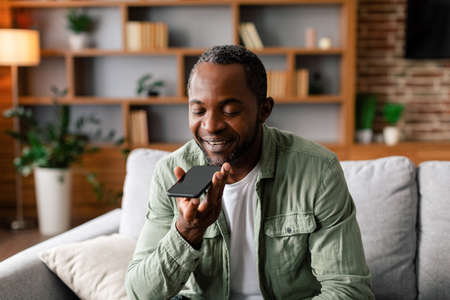 Cheerful middle aged african american male calling by smartphone with blank screen in living room...