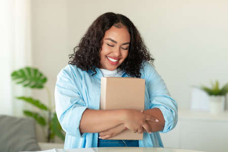 Happy Black Female Buyer Hugging Cardboard Parcel Box At Home