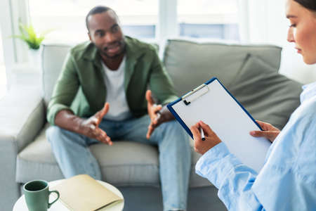 Psychological assistance. African american man having counseling session with therapist at officeの写真素材
