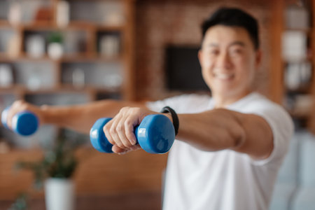 Athlete asian man doing hands exercise with dumbbells in living room interior, doing strength workout at homeの写真素材