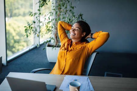 Taking break. Relaxed african american businesswoman resting on chair, leaning back at workplace in officeの写真素材