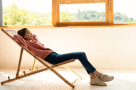 Calm teenage girl relaxing in chair at home, closing eyes and resting on weekend, enjoying the peace and tranquilityの写真素材