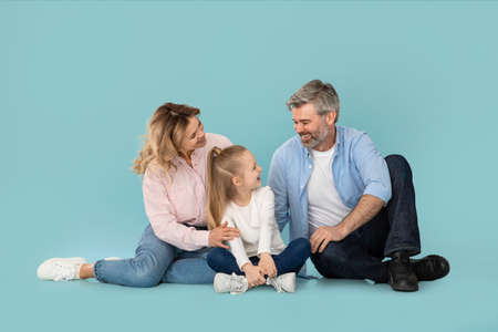 Happy Parents Talking To Little Daughter Sitting Over Blue Backgroundの写真素材