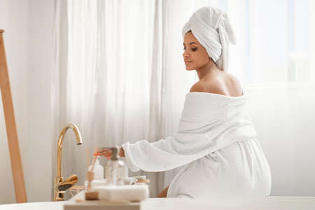 Relaxed Woman Enjoying Bodycare Rituals Using Cosmetics Sitting In Bathroom