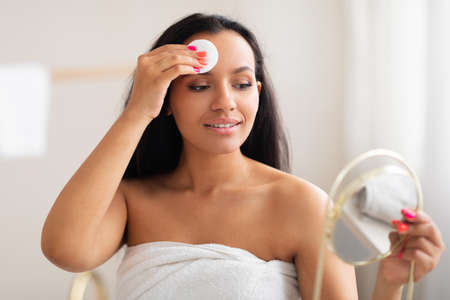 Pretty Woman Using Cotton Pad Cleansing Face Standing In Bathroomの写真素材