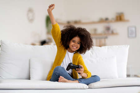 Cheerful little african american kid girl playing video game