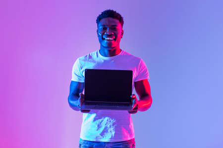 Check this website. Handsome young black man holding laptop with blank screen in neon light, mockup for designの写真素材