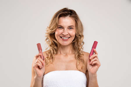 Trendy Makeup. Beautiful middle aged woman holding two lip gloss in hands