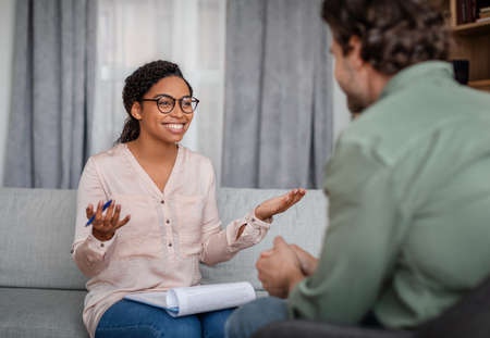 Happy young african american woman doctor in glasses talking with patient at meetingの写真素材