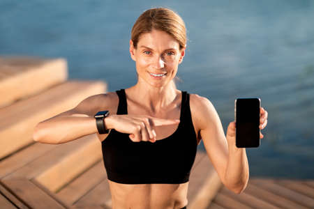 Sport App. Athletic Middle Aged Female Pointing At Blank Smartphone In Handの写真素材