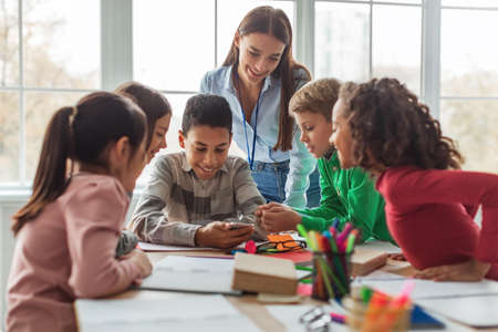 Multiethnic School Kids And Teacher Using Smartphone In Modern Classroom